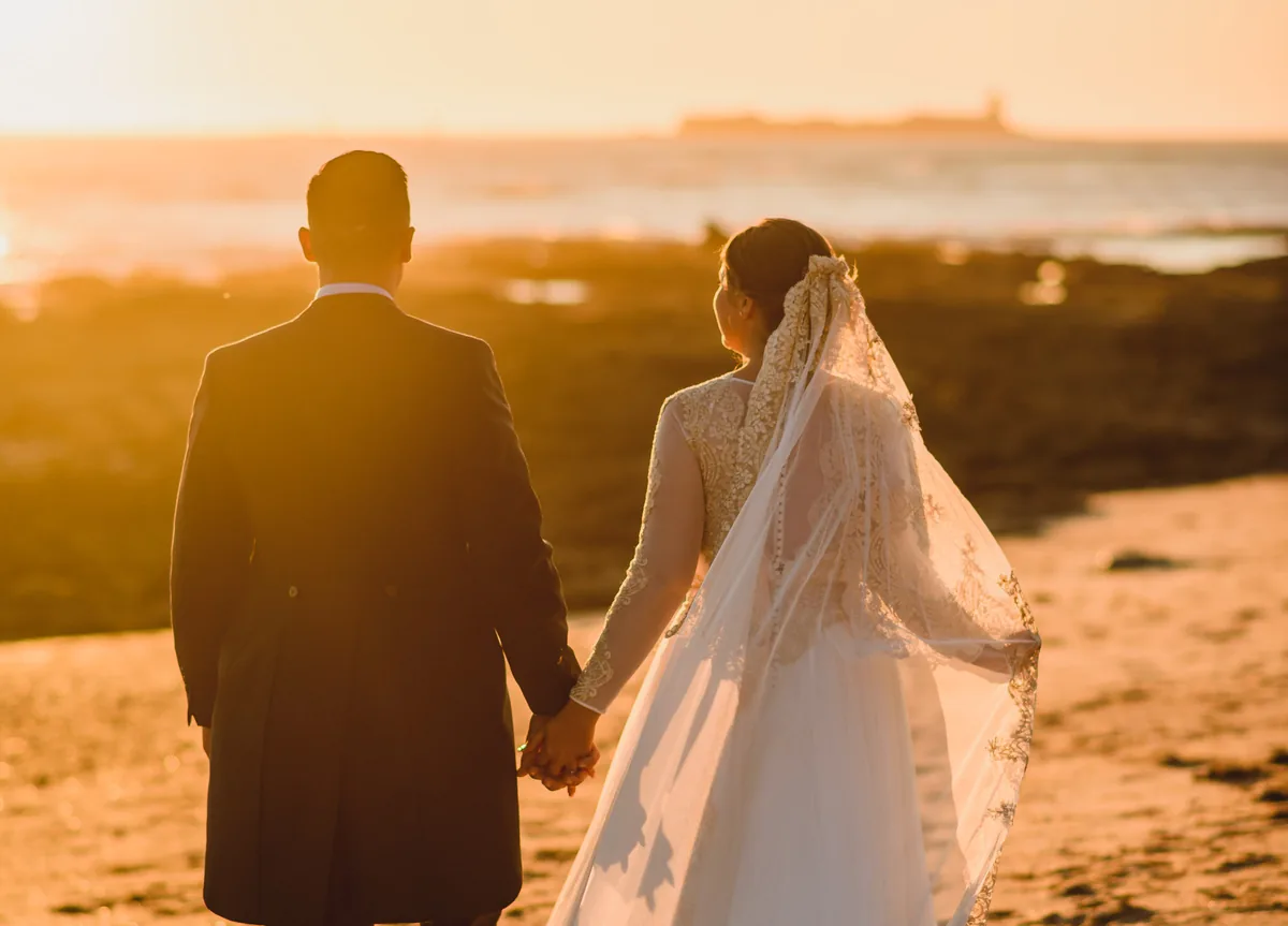 Novios paseando por la playa al atardecer tras la ceremonia